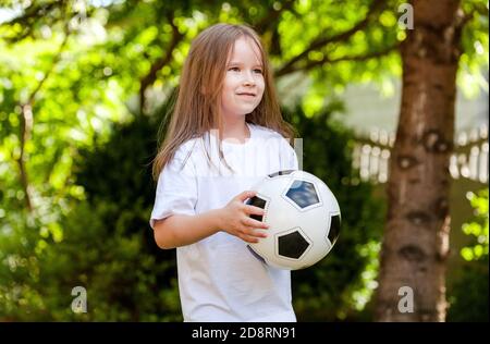 Petite jeune fille d'âge scolaire tenant un simple ballon de football souriant, portrait, été plein air vacances week-end loisirs enfants, sports Banque D'Images