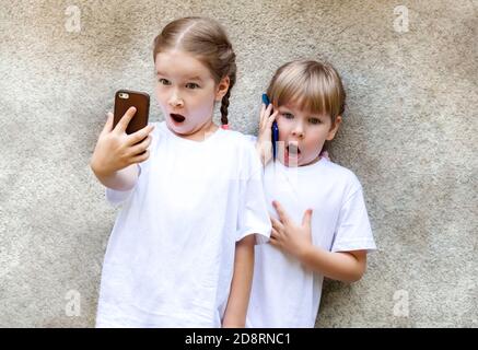 Deux petites filles avec leur téléphone mobile, des enfants excités prenant des selfies avec un smartphone, parlant au téléphone avec surprise expression choquée Banque D'Images