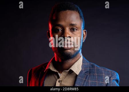 Un homme à la peau sombre portant une chemise de veste regarde l'appareil photo sur un fond noir, regarde l'appareil photo Banque D'Images