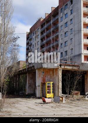 Une cabine téléphonique jaune près d'un immeuble de panneaux à Tchernobyl. Une maison dans une ville fantôme abandonnée. Banque D'Images