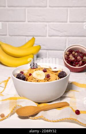 Bol à flocons de maïs avec banane, baies et cuillère en bois sur fond blanc, petit déjeuner sain Banque D'Images