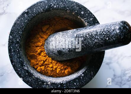 Orange vif d'épice Turmeric dans le mortier de pierre sombre et pilon Banque D'Images