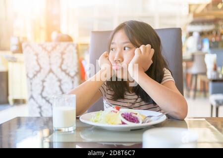 Enfant fille asiatique avec expression de dégoût à l'égard des légumes dans un restaurant, refusant food concept Banque D'Images