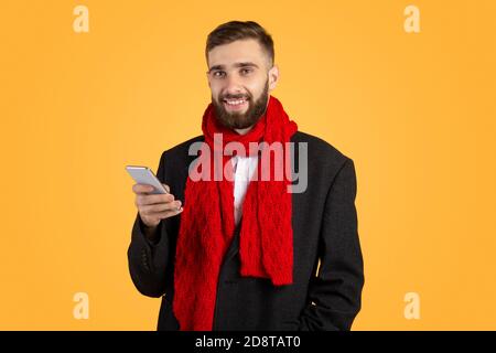 Beau homme d'affaires dans une veste élégante et foulard rouge à l'aide d'un mobile téléphone sur fond orange studio Banque D'Images