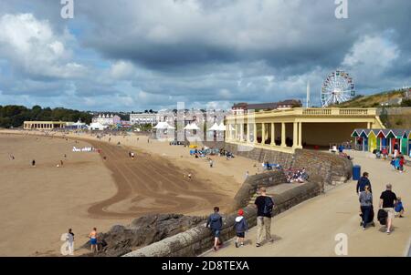 Barry Island, pays de Galles - 6 août 2017 : personnes marchant le long de la promenade avec les pistes d'un tracteur de nettoyage visible sur la plage visible Banque D'Images