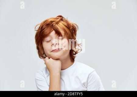 enfant à cheveux rouges avec les yeux fermés tient la main sur le menton court voir sourire Banque D'Images