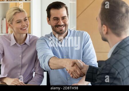 Clients souriants qui se secouent la main avec un agent immobilier masculin à l'intérieur. Banque D'Images