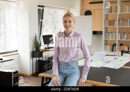 Portrait d'une femme en souriant du millénaire des 25 penchée sur la table. Banque D'Images