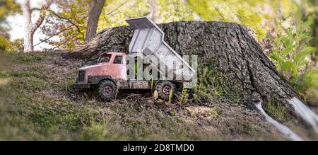 Un camion-benne (jouet) près d'un grand tronc d'arbre coupé presque au niveau du sol. Banque D'Images