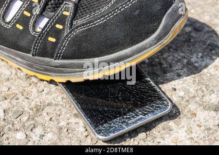 téléphone mobile piétiné posé sur la chaussée sous la chaussure Banque D'Images