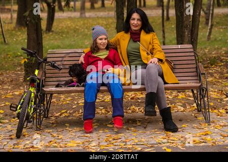 Bonne mère, fils et chien assis sur le banc dans le parc d'automne pour se détendre ensemble Banque D'Images