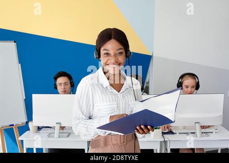 Opérateur de support client noir positif dans le dossier de casque avec documents au centre d'appels Banque D'Images