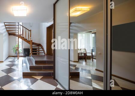Intérieur moderne du hall dans une maison de luxe. Armoire avec miroir. Escalier en bois sombre. Fleur près de la fenêtre. Banque D'Images