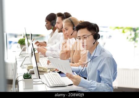 Opérateur de ligne téléphonique asiatique travaillant avec des documents, fournissant des services d'assistance technique aux clients, espace libre Banque D'Images