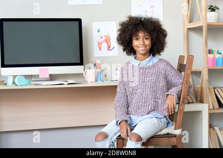 Bonne fille africaine regardant l'appareil photo assis à la maison bureau avec ordinateur. Banque D'Images