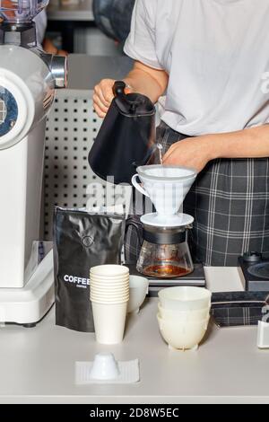 Les mains des femmes du barista préparent le café en versant de l'eau bouillante provenant d'une bouilloire noire dans un entonnoir blanc d'un flacon en verre. Banque D'Images