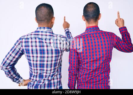 Jeune gay couple de deux hommes portant des vêtements décontractés posant vers l'arrière, en pointant vers l'avant avec le doigt Banque D'Images