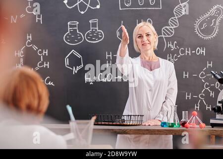 Blonde gai enseignant de chimie en blancoat pointant vers un des écoliers Banque D'Images