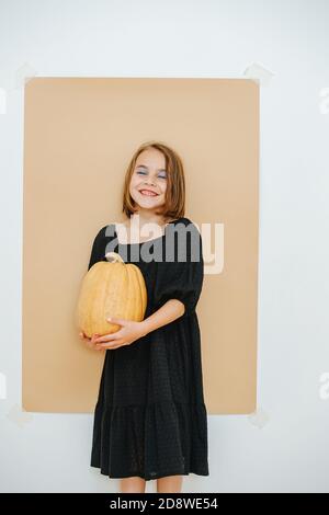 Fille dans un maquillage lourd, robe noire, tenant la citrouille. Vêtu pour halloween. Banque D'Images