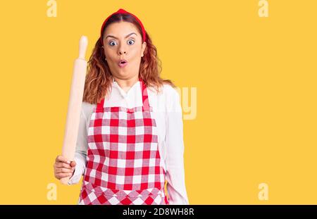 Jeune femme latine portant un tablier tenant le genou effrayé et stupéfié avec la bouche ouverte pour la surprise, incrédulité visage Banque D'Images