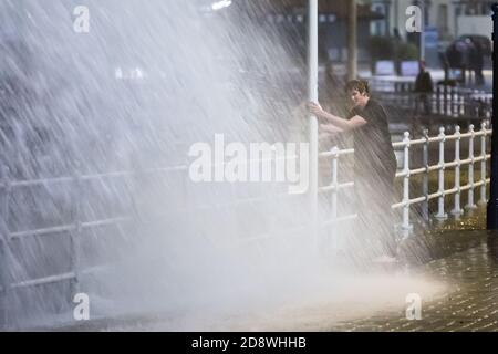 Aberystwyth, Ceredigion, pays de Galles, Royaume-Uni. 1er novembre 2020 Royaume-Uni Météo : un vent fort combiné à une marée haute provoque d'énormes vagues qui se brisent le long de la promenade d'Aberystwyth, alors que deux personnes pendent sur les rampes et postent tout en se trempant. © Ian Jones/Alamy Live News Banque D'Images