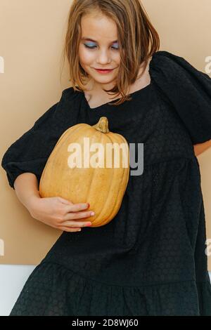 Halloween fille dans un maquillage lourd, robe noire, tenant la citrouille. Banque D'Images