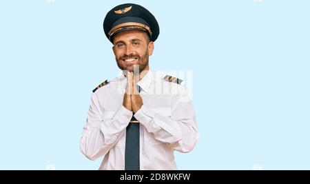 Beau homme avec barbe portant l'uniforme pilote d'avion priant avec les mains ensemble demandant pardon souriant confiant. Banque D'Images