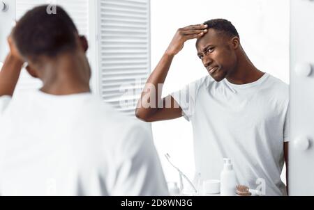 Black Guy examen de sa tête recherche de cheveux gris dans la salle de bains Banque D'Images