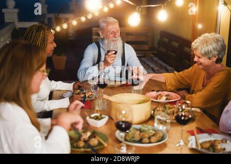 Des personnes âgées ravie de s'amuser au dîner sur le patio - multiracial Amis qui mangent le soir - Focus sur l'homme hippster face Banque D'Images