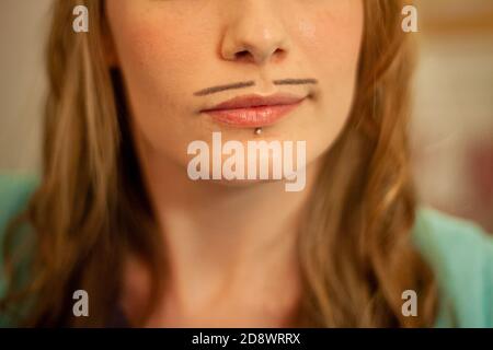 Gros plan sur la partie inférieure de la jeune femme, avec un motif légendaire dessiné sur le visage, la moustache à crayons, pour Movember. Également un perçage de lèvre. Banque D'Images