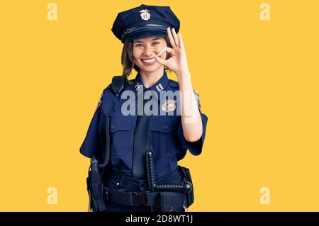 Jeune belle fille portant l'uniforme de police sourire positif faisant signe ok avec la main et les doigts. Expression réussie. Banque D'Images