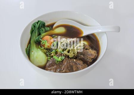 Vue de mise au point sélectionnée à la soupe taïwanaise au bœuf sans nouilles dans un bol blanc sur table blanche. Banque D'Images