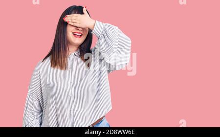 Jeune femme de taille plus portant des vêtements décontractés souriant et riant avec la main sur le visage couvrant les yeux pour la surprise. Concept aveugle. Banque D'Images