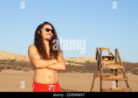 Gros plan d'un jeune homme attrayant avec une longue courbure cheveux portant des lunettes de soleil sur la plage Banque D'Images