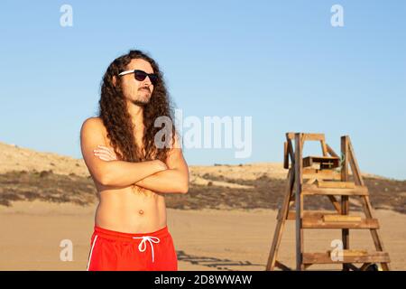 Gros plan d'un jeune homme attrayant avec une longue courbure cheveux portant des lunettes de soleil sur la plage Banque D'Images