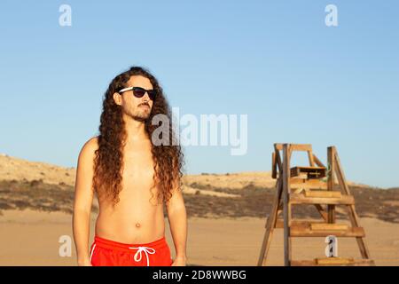 Gros plan d'un jeune homme attrayant avec une longue courbure cheveux portant des lunettes de soleil sur la plage Banque D'Images