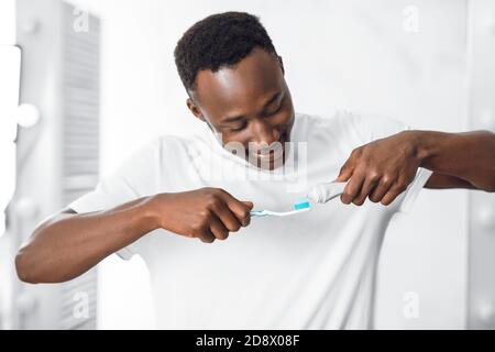 Black Guy appliquant du dentifrice sur la brosse à dents nettoyage des dents dans la salle de bains Banque D'Images