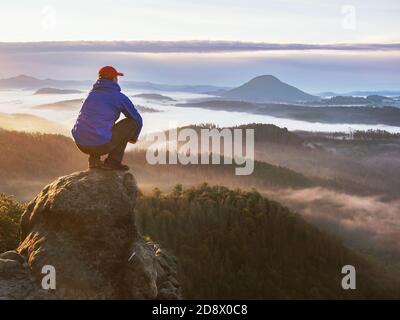 Moment de la pause. L'homme s'assoit sur le rocher et regarde dans la brume colorée et le brouillard dans la vallée. Homme randonnée. Personne triste qui se détend. Banque D'Images