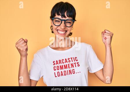Belle femme brunettte portant des commentaires sarcastiques chargement du t-shirt criant fier, célébrant la victoire et le succès très excité avec les bras levés Banque D'Images