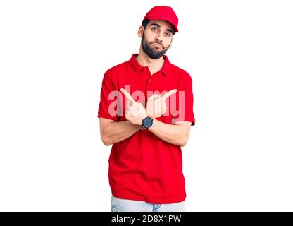 Jeune homme beau avec barbe portant l'uniforme de livraison pointant des deux côtés avec les doigts, direction différente pas d'accord Banque D'Images