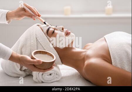 Soin du visage. Esthéticienne appliquant le masque facial en argile à la femme asiatique au spa Banque D'Images