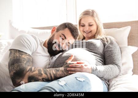 l'homme s'est penché contre la bosse de bébé de sa femme enceinte, qui est couché sur le lit Banque D'Images