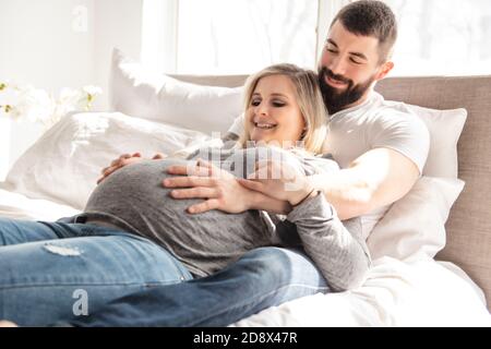 l'homme s'est penché contre la bosse de bébé de sa femme enceinte, qui est couché sur le lit Banque D'Images