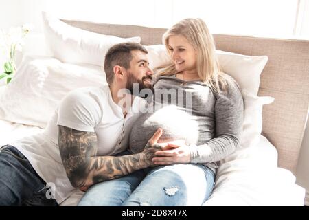 l'homme s'est penché contre la bosse de bébé de sa femme enceinte, qui est couché sur le lit Banque D'Images