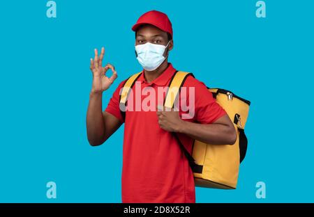 Homme de livraison afro-américain dans un masque médical portant un sac thermo Banque D'Images