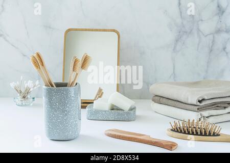 Concept zéro déchet. Ensemble d'accessoires de salle de bain écologiques - brosses à dents en bambou, boutons en coton, brosse à cheveux naturelle, miroir et serviettes en lin. Style de vie durable. Banque D'Images