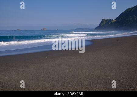 La faible lumière du soleil de l'est capture des vagues se brisant sur une plage de sable au parc national de Humbug Mountain, Oregon. Banque D'Images
