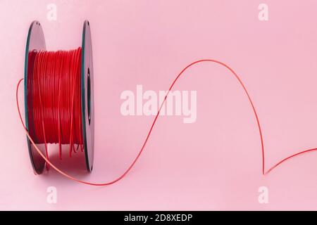Filament en plastique pour imprimante 3D. Bobine de fil thermoplastique rouge pour impression 3D, isolée sur fond rose Banque D'Images