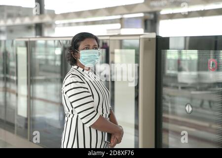Femme portant un masque de visage debout et attendant le train à plate-forme de métro Banque D'Images