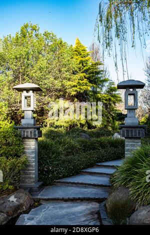 Sentier en pierre sinueux avec piliers chinois, saule pleurant, arbustes contre le ciel bleu Banque D'Images